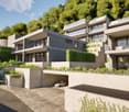 Modern multi-story apartment building with clean, minimalist design. The building has a garage and parking spaces on the ground level. The exterior features a mix of concrete and glass, with balconies and terraces overlooking the surrounding greenery.