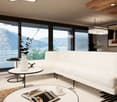 Spacious living room with large windows offering a scenic view of the mountains and lake. The room features a white sofa, a round coffee table, and a modern lighting fixture. The decor has a minimalist and contemporary style with wooden accents.