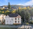 Single family house on hill, surrounded by other houses and trees, one car parked