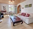 living room with white couch, wooden coffee table, glass table, wooden chairs, wooden desk, flower vase, picture frames, chandelier