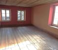 Empty room with wooden floor, red and beige painted walls, two windows with wooden frames