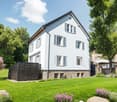 2 story house, white exterior, raised ground floor, large windows, garden, trees, flowers