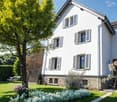 2 story house, white exterior, gray roof, large windows, garden, tree, flowers, lounge chairs