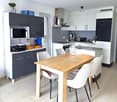 modern kitchen with dining area, wooden table, white chairs, white cabinets, black microwave, printer, blackboard, potted plant, wine bottle, toaster, coffee machine, kettle, sink, gas stove