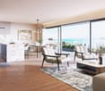 Open plan living room and kitchen, large windows, wooden floor, modern furniture, balcony, sea view