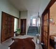 The image shows the entryway of a home. It has a wooden front door, a tiled floor, and a staircase leading up to the second floor. There is a plant and a decorative lantern in the entryway, as well as a 'Happy' sign on the wall. The walls are painted a li