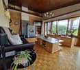 Spacious living room with wooden ceiling, large windows providing a scenic view, leather sofa, wooden cabinets and shelves, and a stone fireplace
