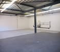 Large open space with concrete floor, metal beams and supports, and overhead lighting. There appears to be a utility or plumbing setup on the wall, suggesting this could be a warehouse or storage facility.