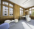 modern office space with large windows, wooden wall paneling, white desks, office chairs, radiator, plants, and grey carpet