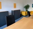 Meeting room with black and yellow chairs, desks, cabinets, plant, and motivational posters on the wall.