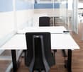 Two desks, glass walls, two black chairs, one of them adjustable, wooden floor.