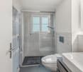 modern, white tiles, glass walk-in shower, white toilet, vanity with a sink, modern faucet, storage cabinet