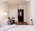 Single bedroom with desk, lamp, chair, wardrobe, double bed, white sheets, grey blanket, bedside table, book, wooden floor
