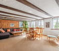 Wooden beams, wooden flooring, sectional sofa, dining table, dining chairs, coffee table, wooden cabinet, radiator, windows with white curtains, picture frame, potted plant