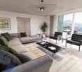large gray sofa, coffee table, two armchairs, large windows with view of mountains, ceiling lamp, rug