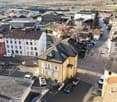 Aerial view of a neighborhood with various buildings, cars parked on the side of the road, and a car park in front of a yellow building.