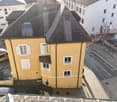 Apartment building, yellow exterior, 3 floors, balcony on 2nd floor, car parking spaces, snow-covered area in the distance
