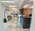 tiled floor, white walls, ceiling lights, a bench and sofa, a water dispenser, a black trash can, a reception desk with a black surface