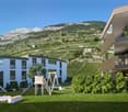 Apartment buildings with multiple levels and balconies, a playground, and a sloped landscape with a vineyard.