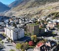 Cityscape with multiple buildings, surrounded by mountains, parking lot, green roofs, terraced fields.