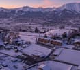 Multiple buildings, covered in snow, set in a mountainous area with a valley