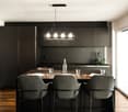 modern kitchen with black cabinets, wooden floor, large island with bar stools, pendant light, glass tableware, plant on countertop