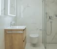 modern bathroom with white marble tiles, wooden cabinet, white sink, modern shower, white toilet