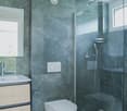 modern bathroom with gray marble walls, white toilet, glass shower enclosure, white sink, wooden cabinet, silver fixtures
