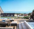 A wooden deck with furniture, a pool, plants, and a view of the town