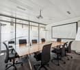 modern meeting room with a long wooden table, black chairs, a white screen, a projector, a whiteboard, and a projector stand