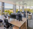 modern office with large windows, multiple desks with monitors, office chairs, office furniture, plants