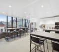 large kitchen table, kitchen cabinets, microwave, refrigerator, garbage bin, sink, chairs, glass windows
