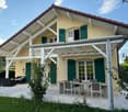 2 story yellow house, red roof, green shutters, outdoor dining table, large balcony
