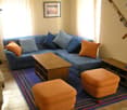 living room, blue sofa, wooden coffee table, blue rug, two orange footstools, two large cushions, fireplace
