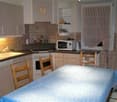 Modern kitchen with a dining area, stove, microwave, sink, dishwasher, wooden chairs, tile flooring