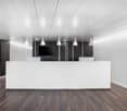 White ceiling, white walls, wooden floors, large white reception desk, monitors, black partition with monitor and printer