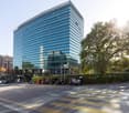 High-rise office building, glass exterior, multiple levels, modern architecture, surrounding greenery, multiple cars parked