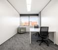Bright and modern office space with large windows, white walls, gray carpet flooring, a desk, an office chair, and a small armchair.