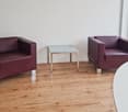 modern room with two chairs, a table, and a white wall with windows