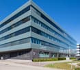 modern office building, glass windows, steel structure, entrance with bollards, parking area, bicycles parked