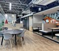 Open concept office space with exposed ceiling beams, modern furniture, and a large fireplace feature. The space includes a dining table with chairs, lounge seating, and storage units along the walls.