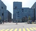 modern office building, glass facade, multiple floors, street view, cars parked, pedestrian crossing, street lights, trees, traffic signs