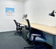 Empty office room with white walls, gray carpet, a desk, 2 office chairs, a plant in a vase, a black lamp, and a picture frame.