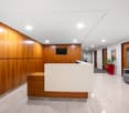 Spacious lobby with wood-paneled walls, white reception desk, tiled flooring, and modern furniture including a sofa and potted plants