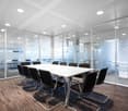 Large conference room with white table, black chairs, glass walls, and recessed lighting in the ceiling