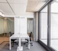 Modern office space with large windows, white walls, concrete ceiling, glass partitions, and a white table with two office chairs.
