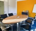 oval conference table, chairs around the table, white board, small storage cabinet, yellow wall, door