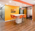Orange wall, white ceiling, a rectangular table with 6 orange chairs, 2 lamps