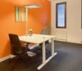 modern workspace with two white standing desks, orange wall, grey swivel chairs, white potted plant