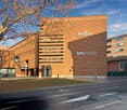 Large brown brick building with the Regus and BPS (SUISSE) logos displayed prominently. The building has a modern, striped facade design and is surrounded by trees and other buildings.